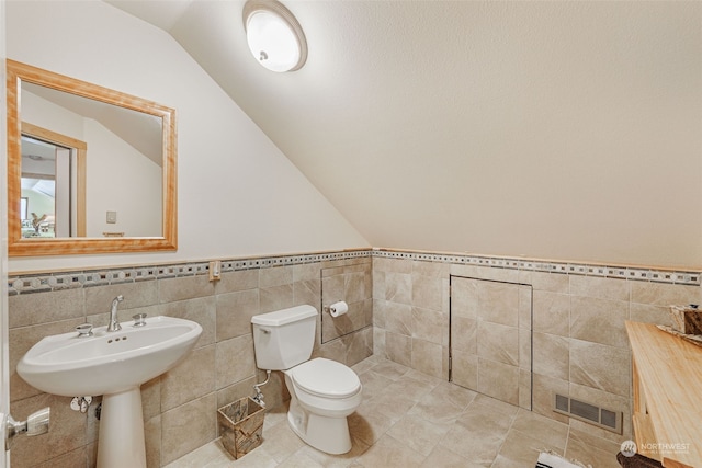 bathroom with lofted ceiling, toilet, tile walls, and tile patterned floors