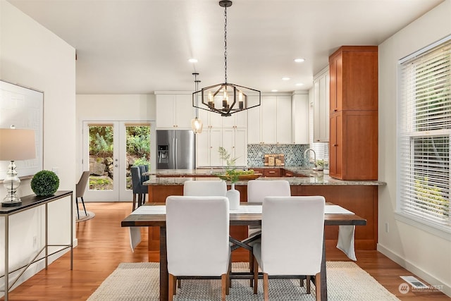 dining space featuring sink, french doors, a notable chandelier, and light hardwood / wood-style flooring