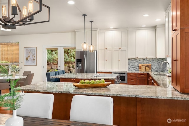 kitchen featuring white cabinetry, sink, wall oven, stainless steel fridge with ice dispenser, and pendant lighting