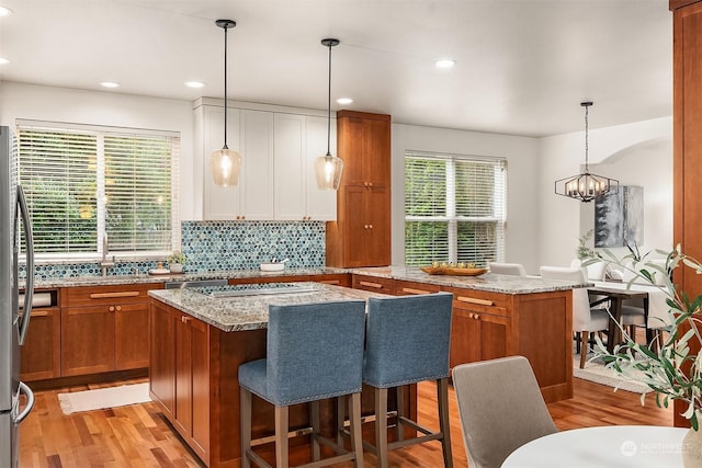 kitchen with light stone counters, light hardwood / wood-style flooring, a kitchen island, and decorative light fixtures