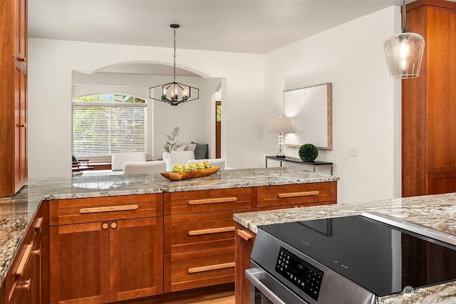 kitchen featuring light stone countertops, stove, an inviting chandelier, and pendant lighting