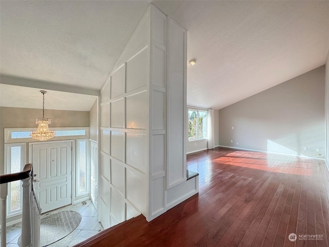 hallway featuring hardwood / wood-style flooring, lofted ceiling, and a chandelier