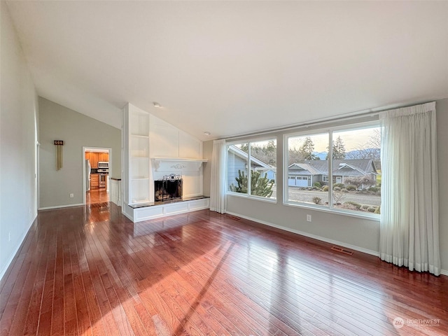 unfurnished living room featuring dark wood-type flooring, a healthy amount of sunlight, and vaulted ceiling