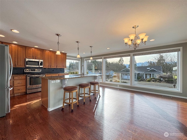 kitchen featuring pendant lighting, appliances with stainless steel finishes, crown molding, and a kitchen island with sink