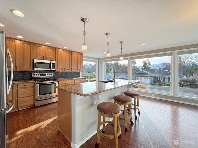 kitchen with appliances with stainless steel finishes, pendant lighting, sink, a kitchen bar, and a kitchen island with sink