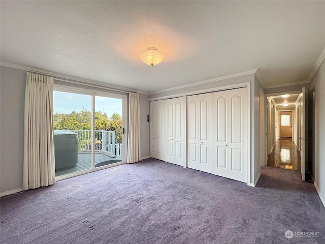 unfurnished bedroom featuring multiple closets, access to exterior, crown molding, and dark colored carpet