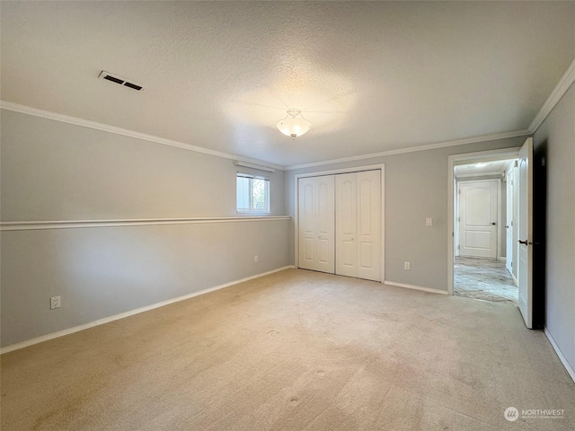 unfurnished bedroom with light carpet, ornamental molding, a closet, and a textured ceiling