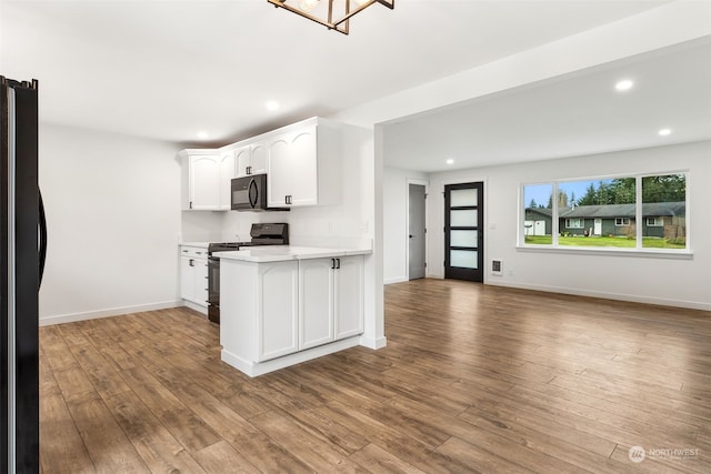 kitchen with white cabinets, light hardwood / wood-style floors, kitchen peninsula, and black appliances