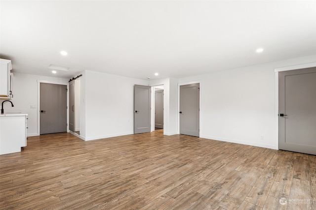 unfurnished living room featuring a barn door, sink, and light hardwood / wood-style flooring