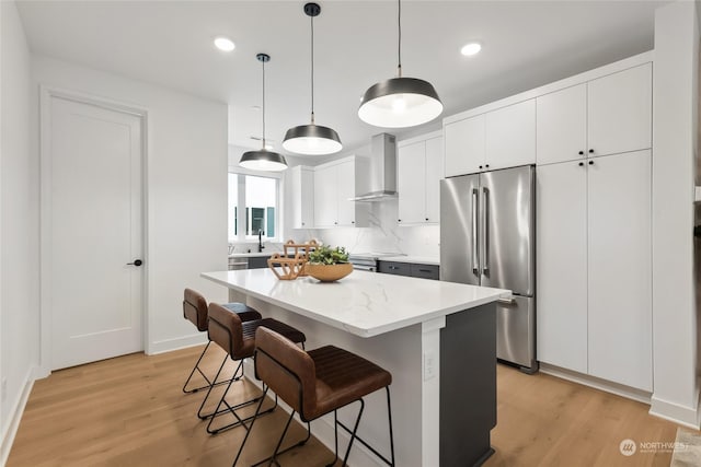 kitchen with pendant lighting, a center island, wall chimney range hood, high quality fridge, and white cabinetry