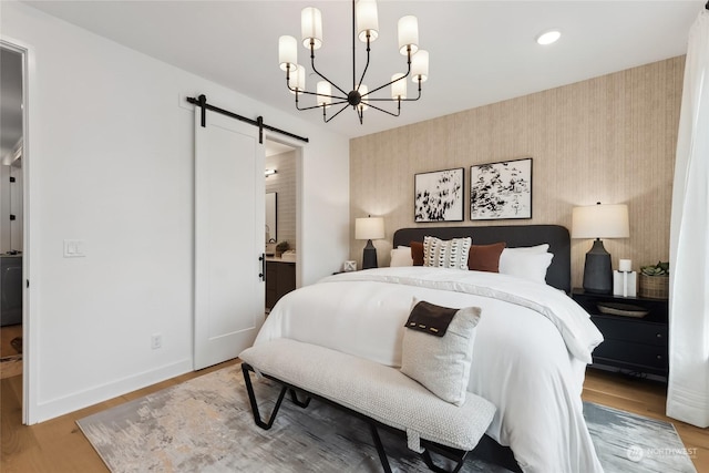 bedroom with hardwood / wood-style flooring, a barn door, an inviting chandelier, and ensuite bath