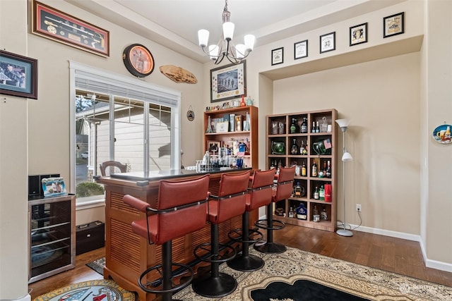 bar featuring wood-type flooring, wine cooler, and an inviting chandelier