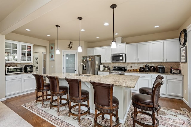 kitchen with white cabinets, pendant lighting, stainless steel appliances, and a kitchen island with sink