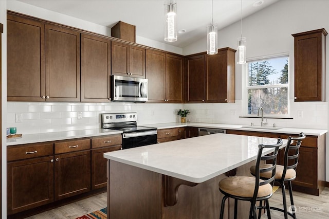 kitchen featuring sink, a center island, stainless steel appliances, light hardwood / wood-style flooring, and decorative light fixtures