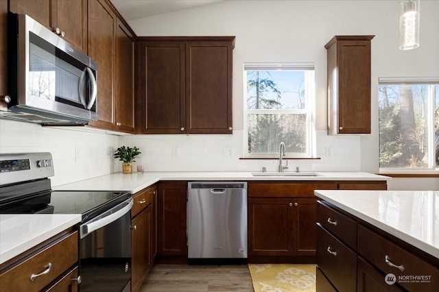 kitchen with light wood-type flooring, stainless steel appliances, sink, hanging light fixtures, and lofted ceiling