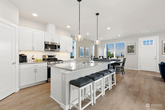 kitchen featuring white cabinetry, hanging light fixtures, stainless steel appliances, a kitchen bar, and a kitchen island with sink