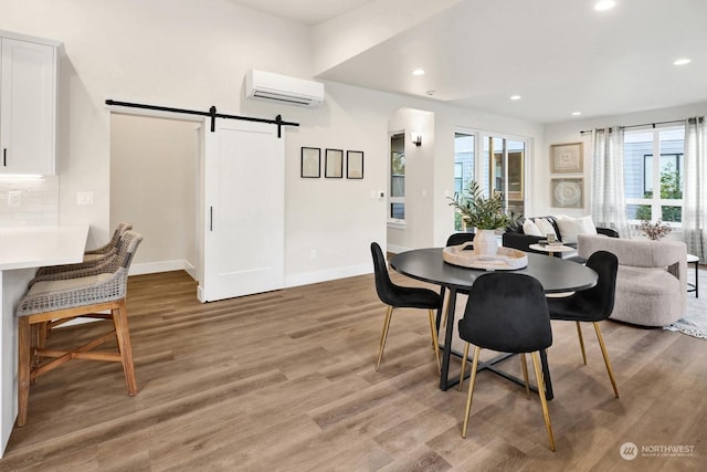 dining space with hardwood / wood-style flooring, a barn door, and an AC wall unit