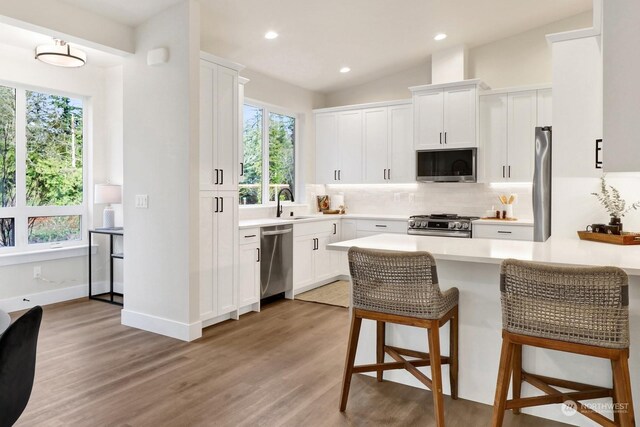 kitchen with appliances with stainless steel finishes, vaulted ceiling, sink, hardwood / wood-style flooring, and white cabinetry