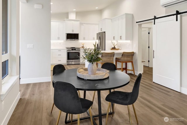 dining space with a barn door, hardwood / wood-style floors, high vaulted ceiling, and a wall mounted air conditioner