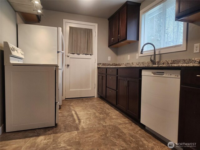 kitchen with dark brown cabinets, white appliances, a sink, and light stone countertops