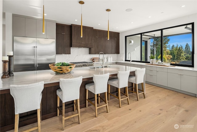 kitchen with a kitchen breakfast bar, sink, built in refrigerator, light hardwood / wood-style floors, and range