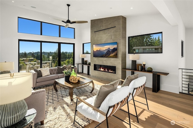 living room with a high ceiling, light hardwood / wood-style floors, ceiling fan, and a tiled fireplace