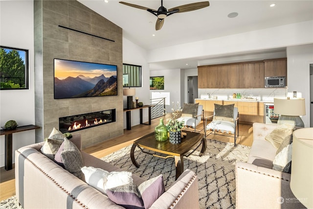 living room with ceiling fan, sink, light hardwood / wood-style flooring, vaulted ceiling, and a tiled fireplace