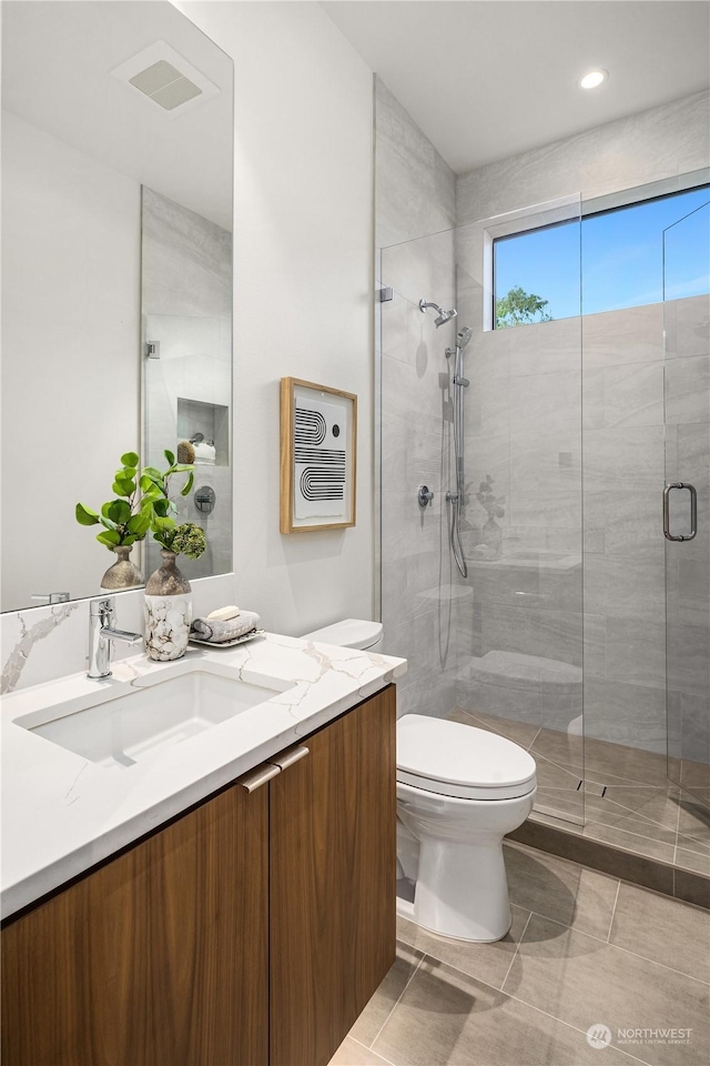 bathroom featuring tile patterned floors, vanity, a shower with shower door, and toilet