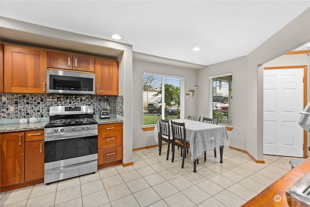 kitchen featuring decorative backsplash, light stone counters, light tile patterned floors, and appliances with stainless steel finishes