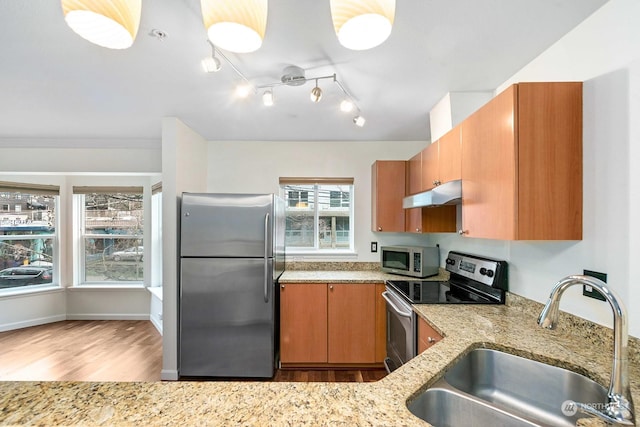 kitchen featuring light stone countertops, sink, appliances with stainless steel finishes, and light hardwood / wood-style flooring