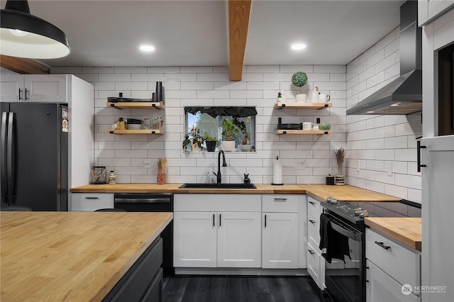 kitchen with wood counters, sink, wall chimney range hood, black appliances, and white cabinetry