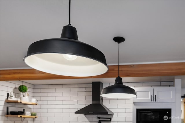 room details with decorative light fixtures, white cabinetry, wall chimney range hood, and tasteful backsplash