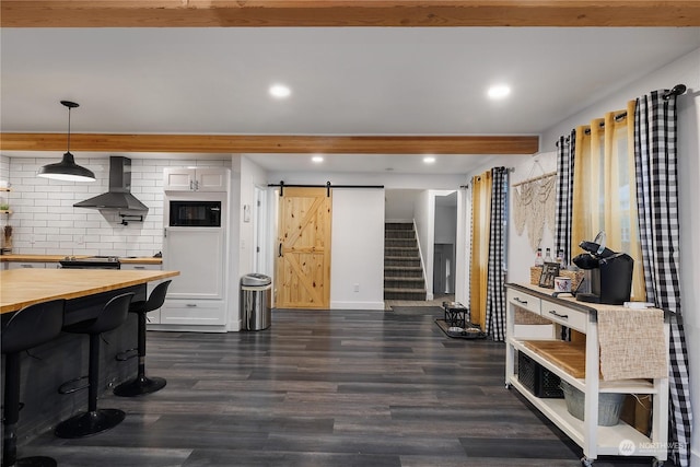 kitchen featuring pendant lighting, dark wood-type flooring, wall chimney range hood, a barn door, and white cabinetry