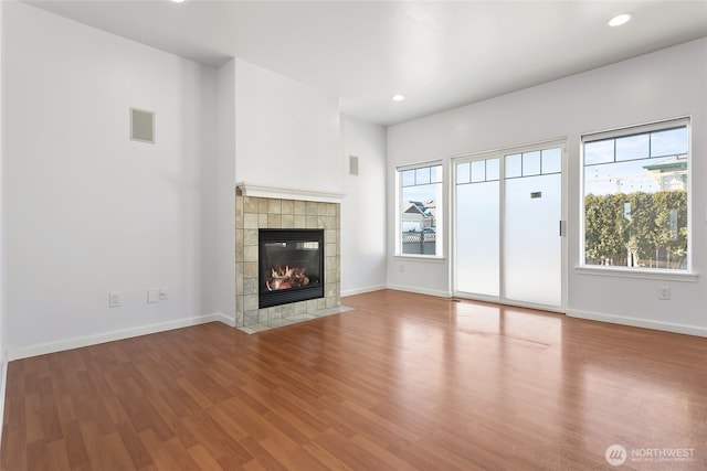 unfurnished living room featuring wood finished floors, plenty of natural light, a tile fireplace, and baseboards