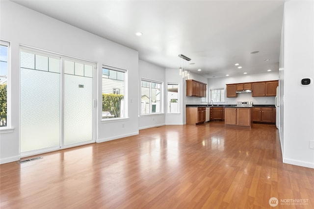 unfurnished living room with light wood finished floors, baseboards, a sink, and recessed lighting