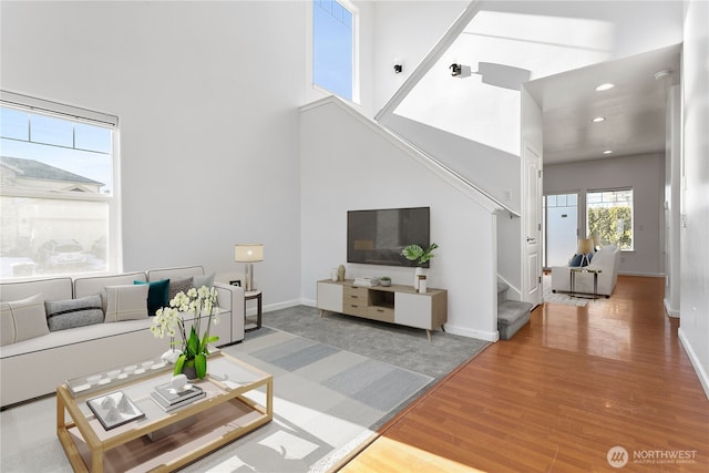 living area with a towering ceiling, baseboards, stairway, and wood finished floors