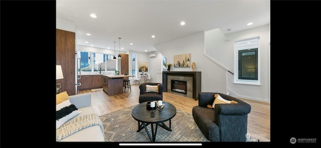 living room with a wall unit AC, a fireplace, and light wood-type flooring