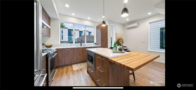 kitchen featuring stainless steel appliances, an AC wall unit, a kitchen bar, light hardwood / wood-style floors, and hanging light fixtures