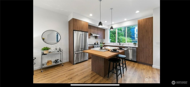 kitchen with a kitchen breakfast bar, light hardwood / wood-style floors, a kitchen island, pendant lighting, and appliances with stainless steel finishes