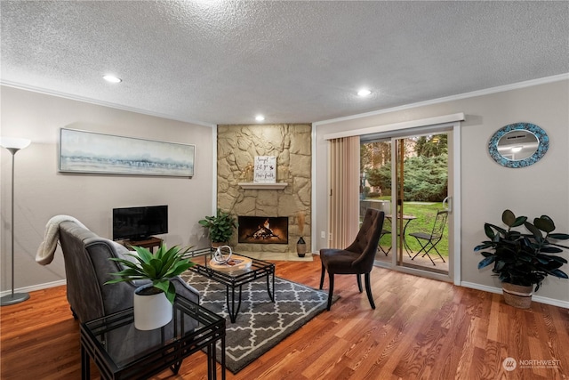 sitting room with crown molding, wood-type flooring, a stone fireplace, and a textured ceiling