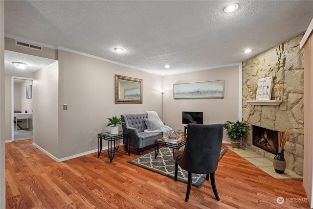 sitting room featuring crown molding, a stone fireplace, a textured ceiling, and light hardwood / wood-style flooring