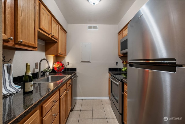 kitchen with sink, light tile patterned floors, stainless steel appliances, and dark stone countertops