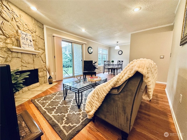 living room featuring a stone fireplace, crown molding, hardwood / wood-style floors, and a textured ceiling