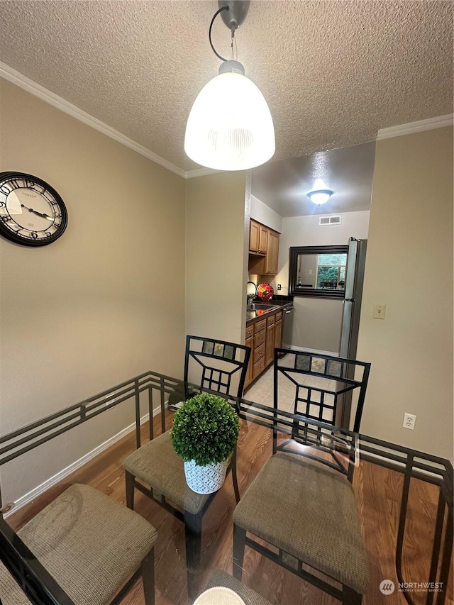 dining space with sink, a textured ceiling, ornamental molding, and light wood-type flooring