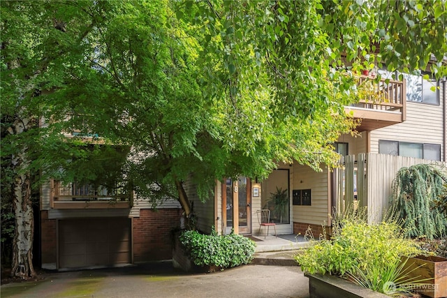 exterior space with brick siding, fence, a balcony, and an attached garage