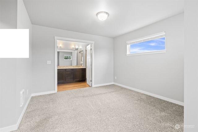 unfurnished bedroom featuring light carpet, ensuite bathroom, and multiple windows