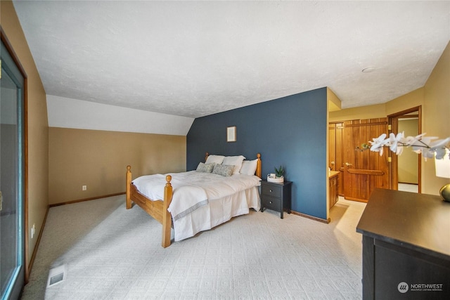 carpeted bedroom featuring a textured ceiling, ensuite bathroom, and vaulted ceiling