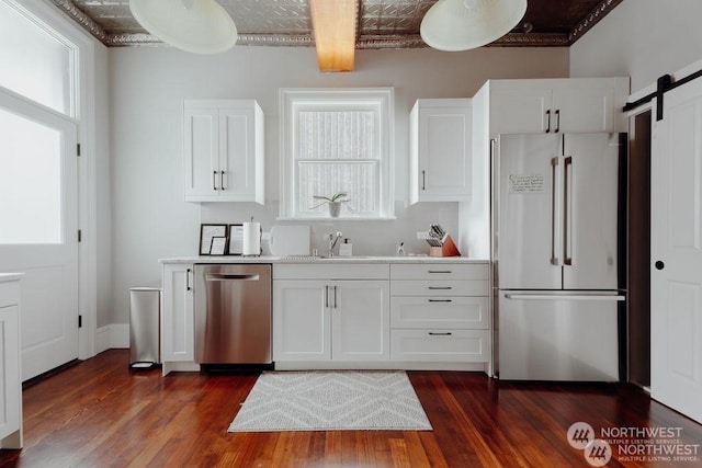 kitchen featuring white cabinets, appliances with stainless steel finishes, a barn door, and dark hardwood / wood-style flooring