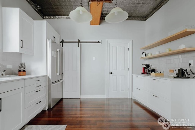 kitchen with high quality fridge, a barn door, pendant lighting, and white cabinetry