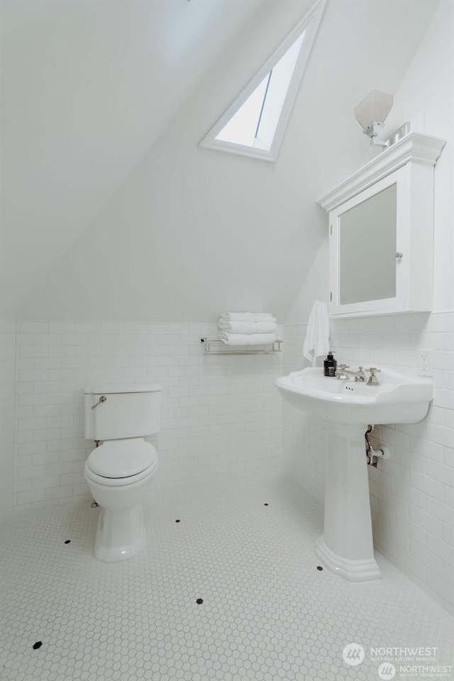 bathroom featuring tile walls, lofted ceiling with skylight, tile patterned floors, and toilet